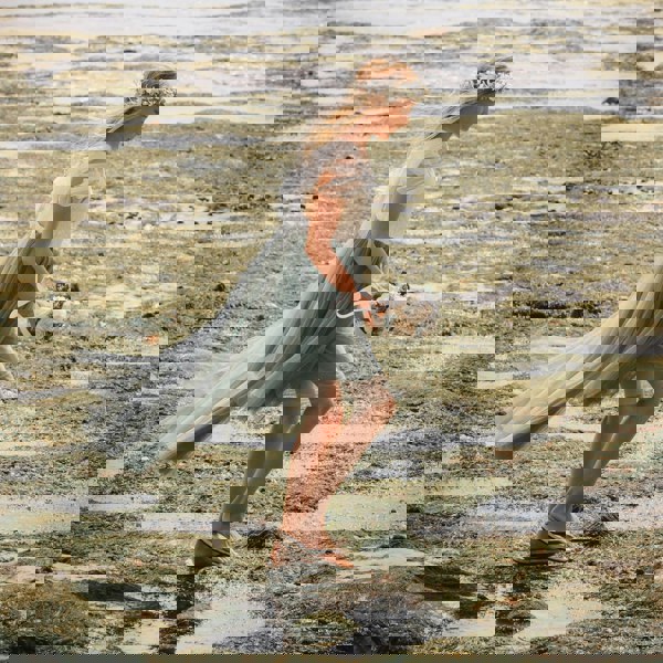 Girl in a flowing dress from UK Flower Girl Boutique walking on a beach with a bouquet.