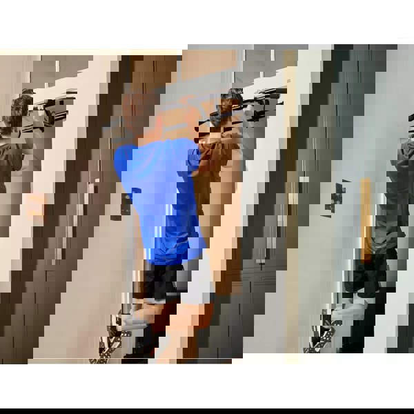 Person using a pull-up bar attached to a door frame for exercise.