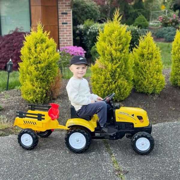 Yellow ride-on tractor toy with orange front shovel, four wheels, and rear trailer