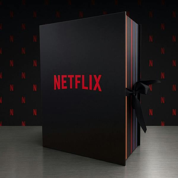 A large, premium matte black advent calendar box styled like a thick book with the bold red 'NETFLIX' logo across the front, secured with a black satin ribbon on a metallic surface against a dark background with faint red N patterns.