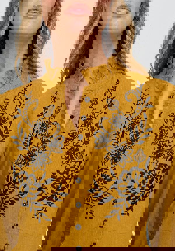 Mustard yellow blouse with black floral embroidery on a white background