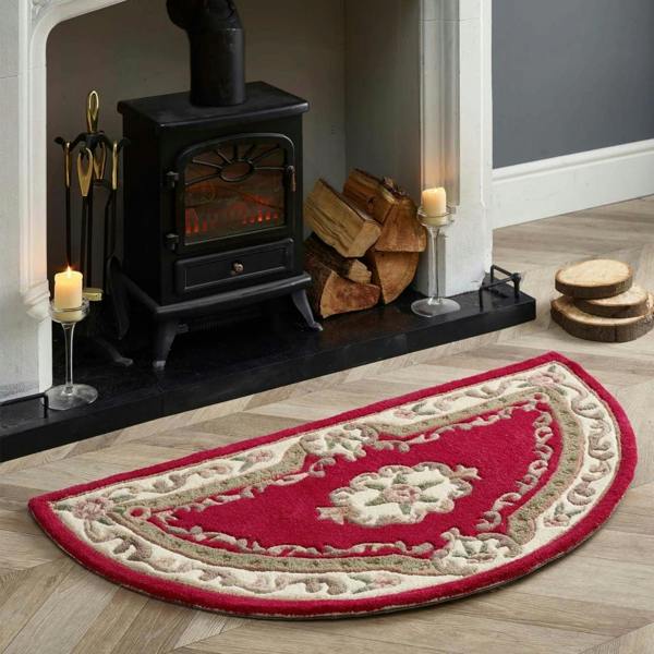 Decorative red and beige rug in front of a fireplace with logs and candles.