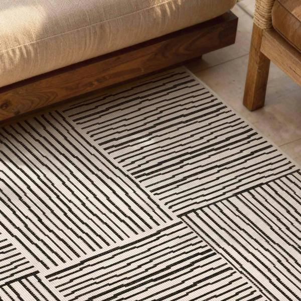Patterned rug with black lines on a beige floor next to wooden furniture.