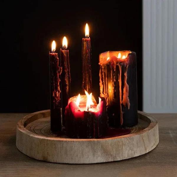 Four lit black taper candles with red wax drips on round wooden holder