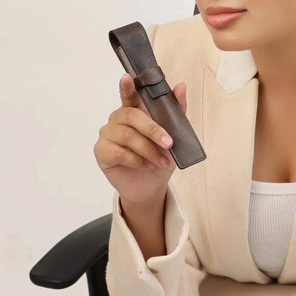 Person holding a brown leather pen holder against a neutral background