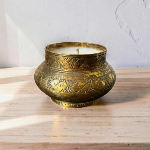 Decorative brass candle holder with a lit candle on a wooden surface.