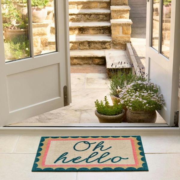Doormat with 'Oh hello' text in front of a house entrance with plants and steps.