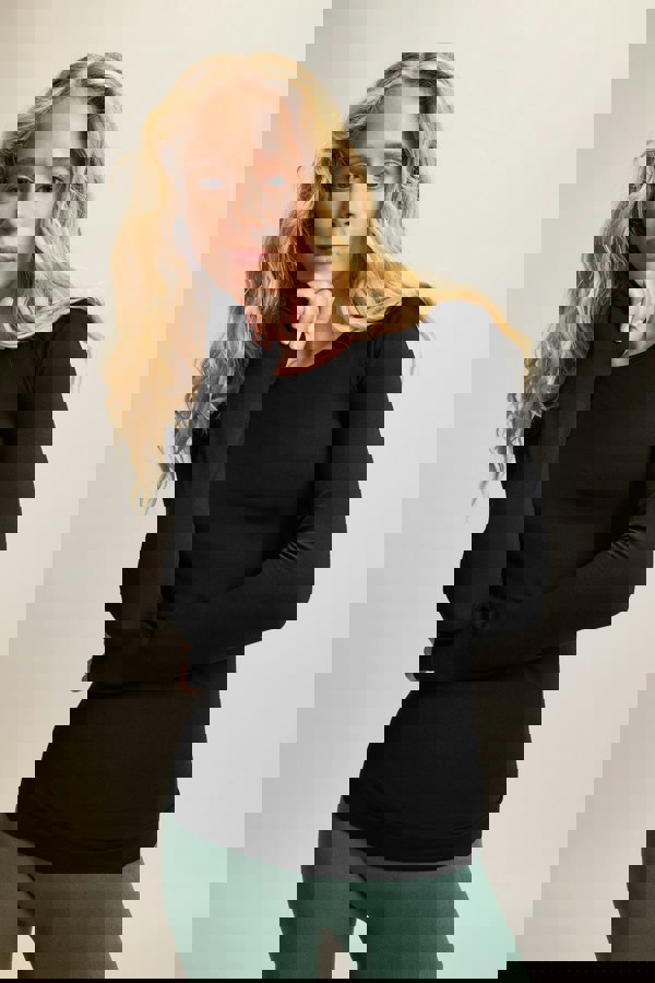 Model wearing a black long-sleeve top made from moisture-wicking fabric, paired with high-waisted green leggings. The sleek, seamless design of the lightweight and breathable long-sleeve top, featuring thumbholes, makes it perfect for yoga and athleisure wear. Ideal for activewear enthusiasts seeking stylish and sustainable workout gear, this outfit combines high-performance sportswear with versatile, all-day comfort. Suitable for a variety of activities, from intense workouts to casual athleisure looks