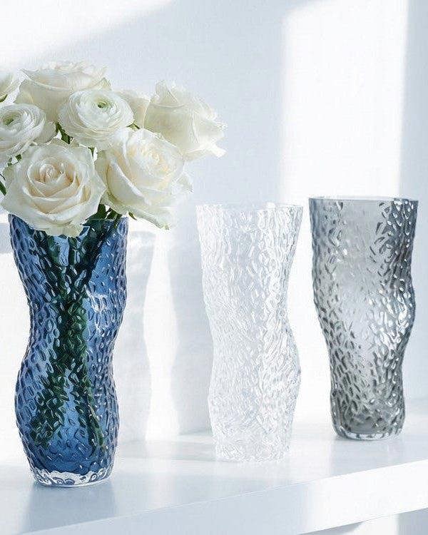 Three textured vases in blue, clear, and grey on a light background