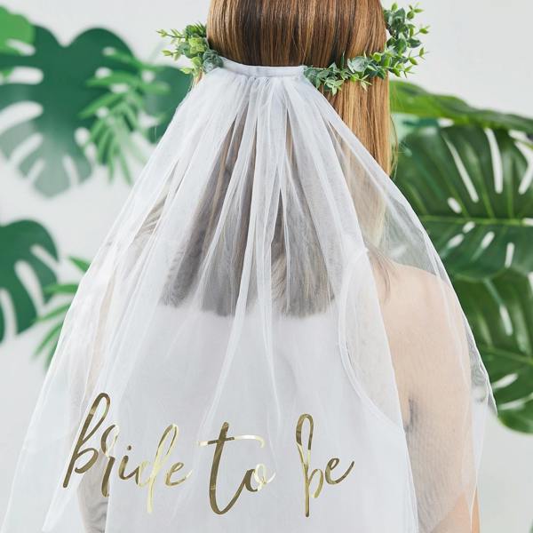 Rear view of a bride wearing a faux green eucalyptus foliage leaf crown headband with a flowing white tulle veil featuring gold-foiled cursive Bride to Be text.