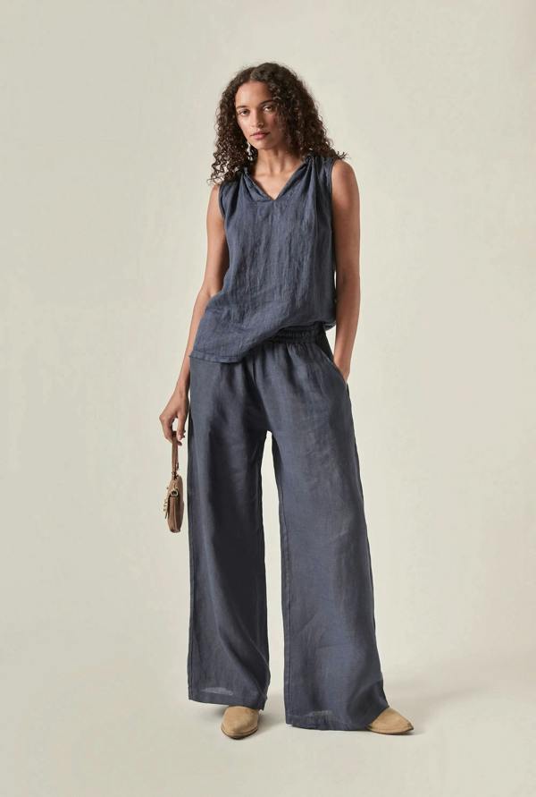 Woman wearing a sleeveless navy linen  top and wide-leg pants on a plain background