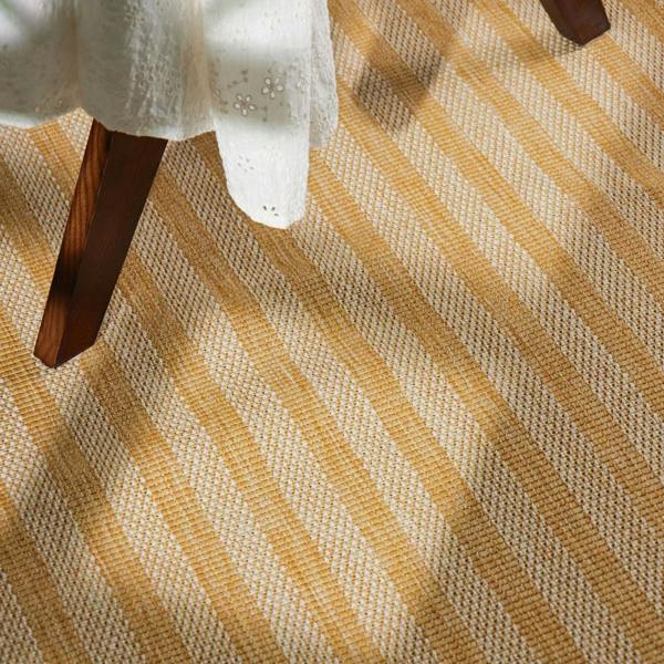 Close-up of a textured yellow and beige rug with a wooden chair leg.