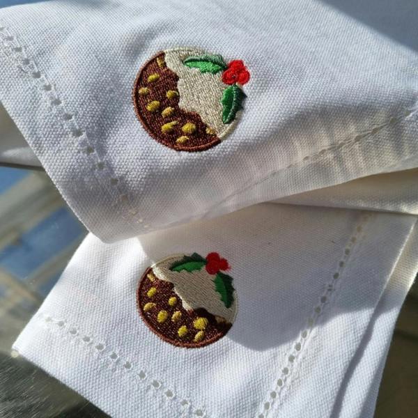 Hand-embroidered white linen napkin featuring a blue brown sauce bottle design and purple scalloped edge on a wood background.