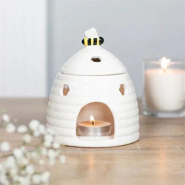 White ceramic beehive oil burner with tealight flame and bee-pattern lid
