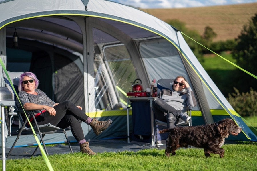 A male, female and a dog sat outside of the OLPRO Odyssey  Breeze® Inflatable 8 Berth Tent.