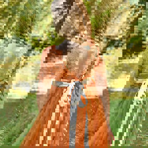 Child in an orange dress with a white belt standing in a natural setting