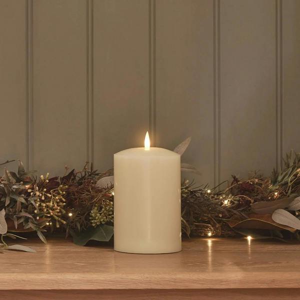 15cm ivory LED chapel candle with a realistic flame on a wooden shelf with fairy lights.