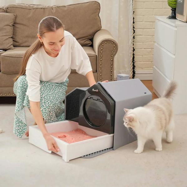 Grey enclosed cat litter box with open pull-out drawer; person refilling litter.