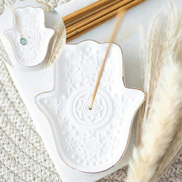 White hamsa hand incense holder with incense stick inserted and embossed pattern