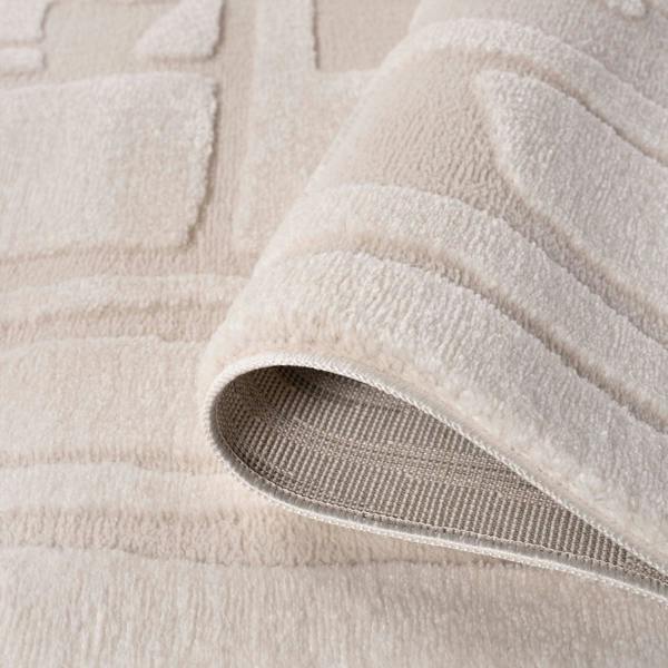 Close-up of a beige textured rug with a slight roll-up showing the underlayer.