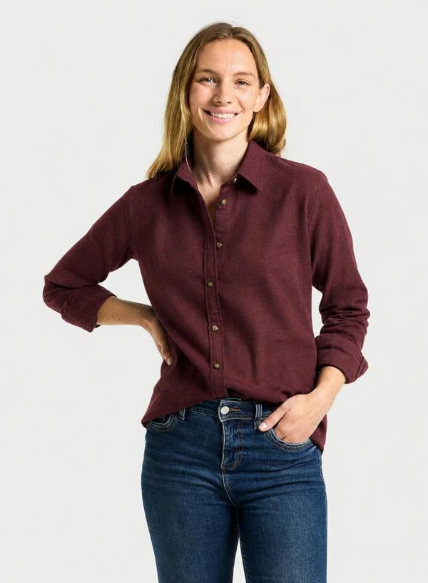 A woman wearing a long-sleeve button-up shirt in maroon and blue jeans, standing against a light gray studio background.