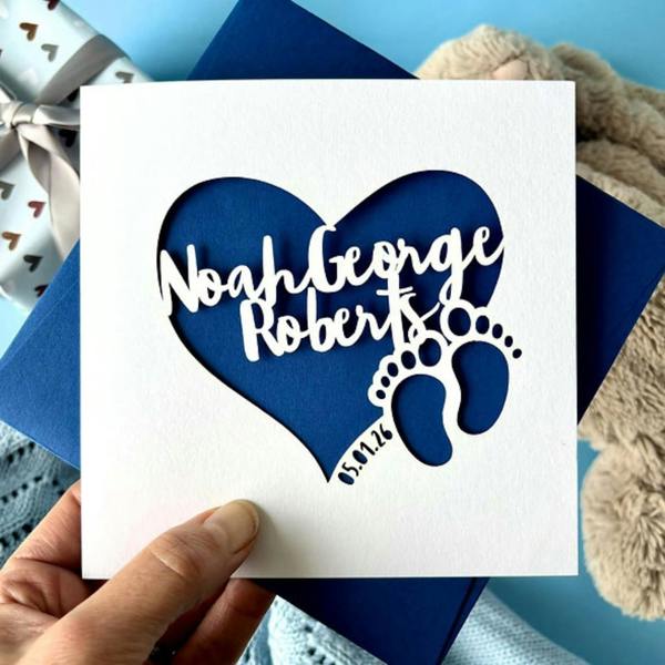 Square white papercut heart new baby card personalised with the name Noah George Roberts and birth date against a royal blue insert