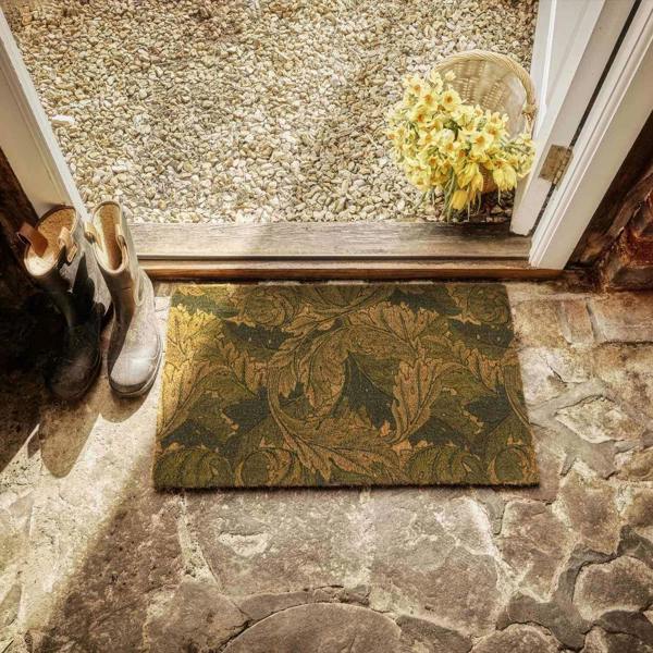 Doormat with leaf pattern on stone floor, shoes, and basket of flowers.