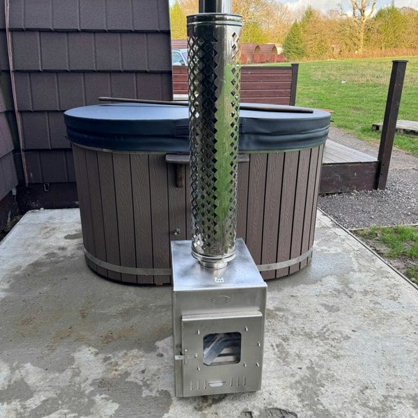 Wood-fired hot tub on a wooden platform with a scenic sunset over mountains and fields.