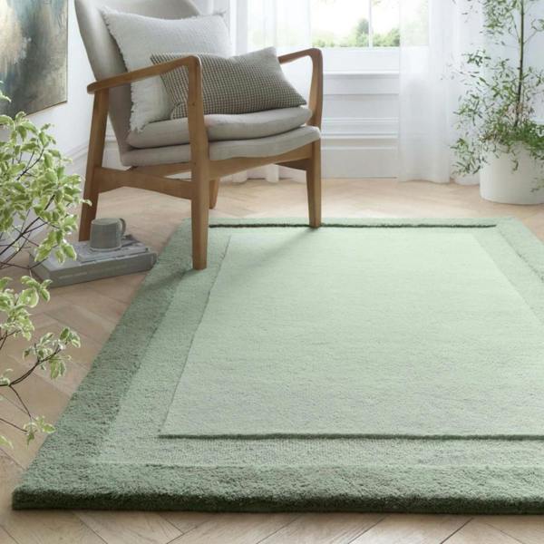 Green rug on a wooden floor with a chair and plants in a room.