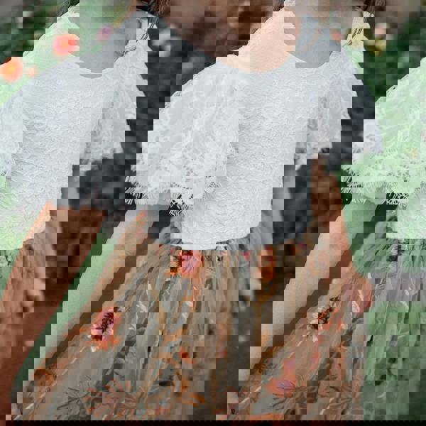 Child wearing a white lace top and floral skirt with a garden background