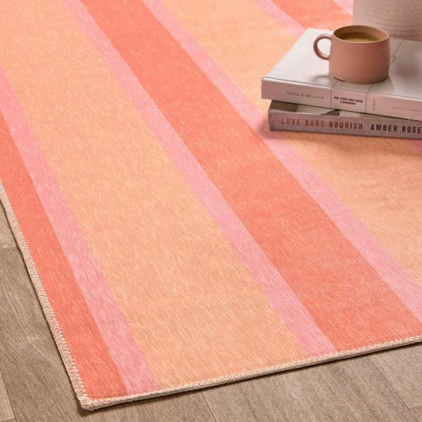 Striped pink and orange rug on a wooden floor with books and a mug.