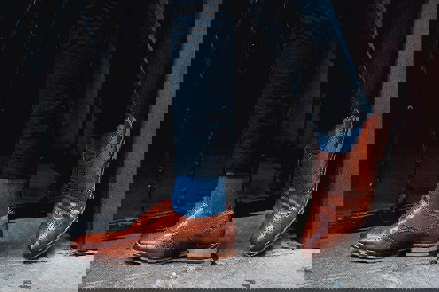 Brown leather shoes worn with blue socks on a dark background