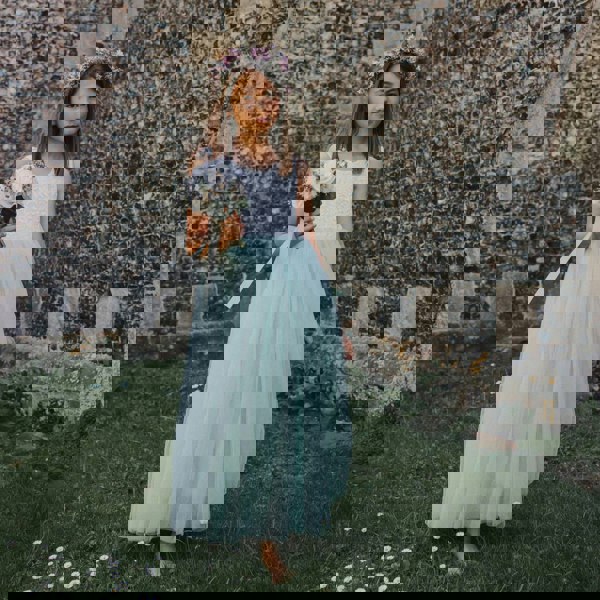 Young girl in a light blue dress holding flowers against a stone wall.