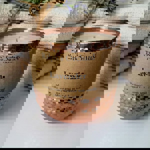 Candle in a copper container with 'Ralph's Orchard' label on a white surface