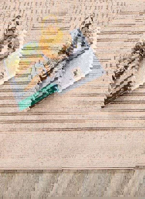 Abstract striped geometric rug in neutral tones with decorative vase and magazine on wooden floor.