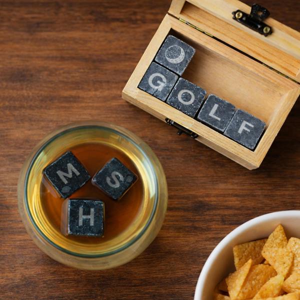 Overhead view of personalised whisky stones in a glass and a wooden box spelling GOLF.