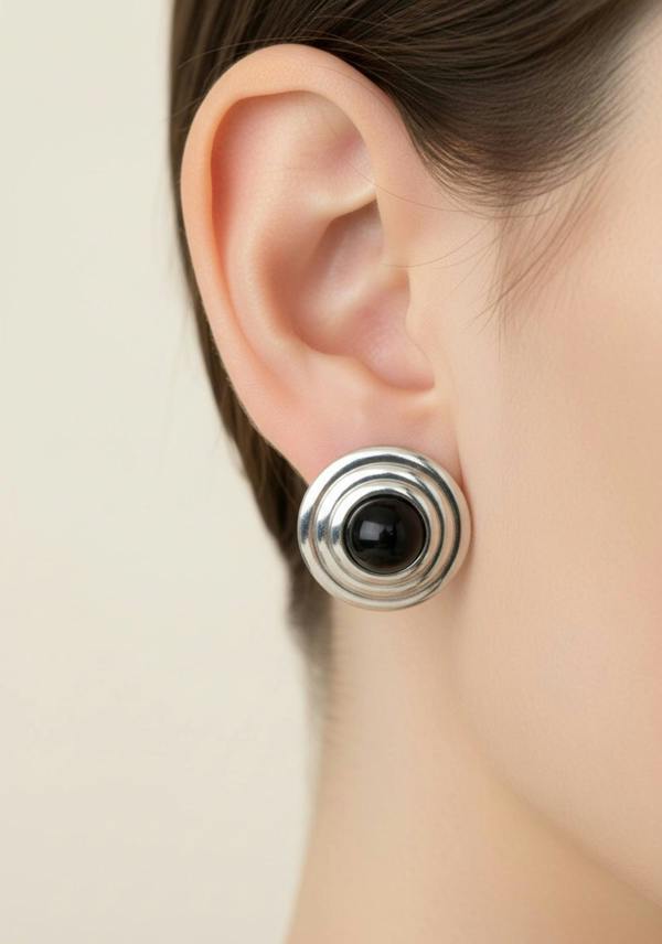 Close-up of an ear wearing a silver and black earring against a neutral background