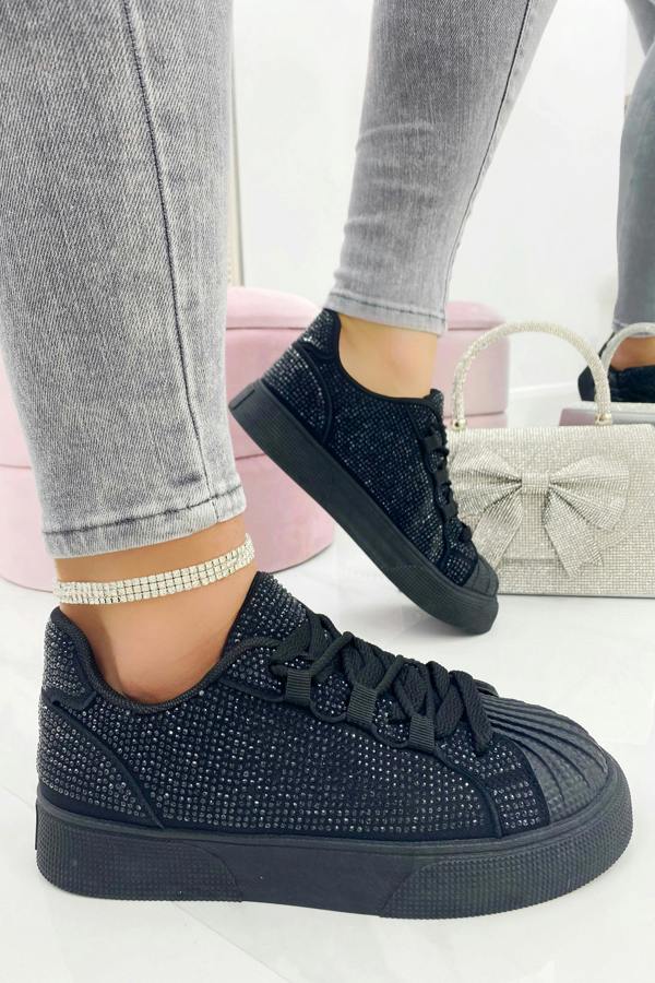 Black embellished sneakers worn with gray jeans on a white background