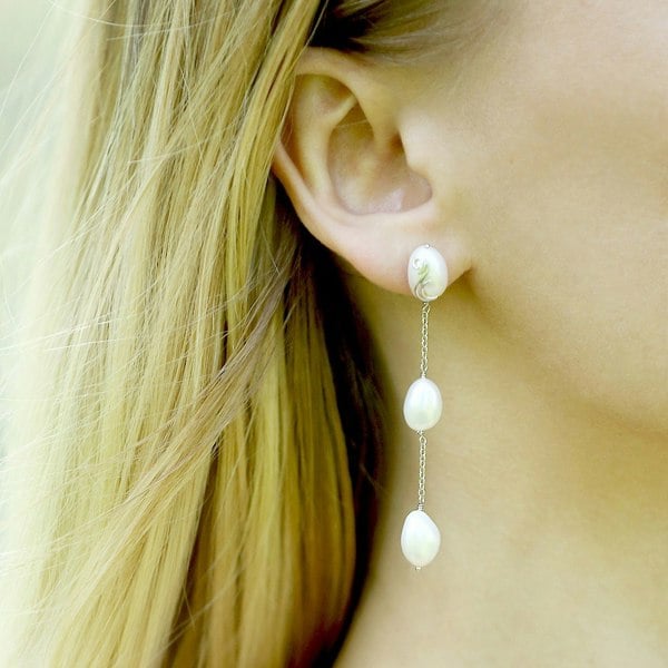 Triple freshwater pearl dangle earrings on an ear.