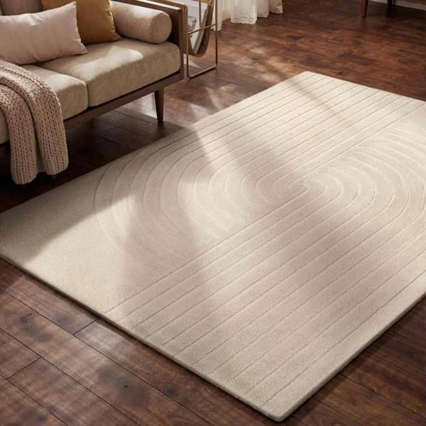 Beige area rug on a wooden floor with a couch in the background