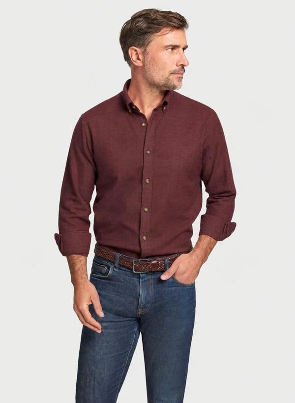 A man wearing a long-sleeve button-down shirt in maroon and blue jeans, standing against a light gray background.