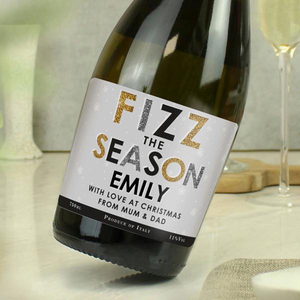 Personalised Fizz The Season Prosecco bottle displaying custom name EMILY on a festive snowflake label next to a champagne flute.