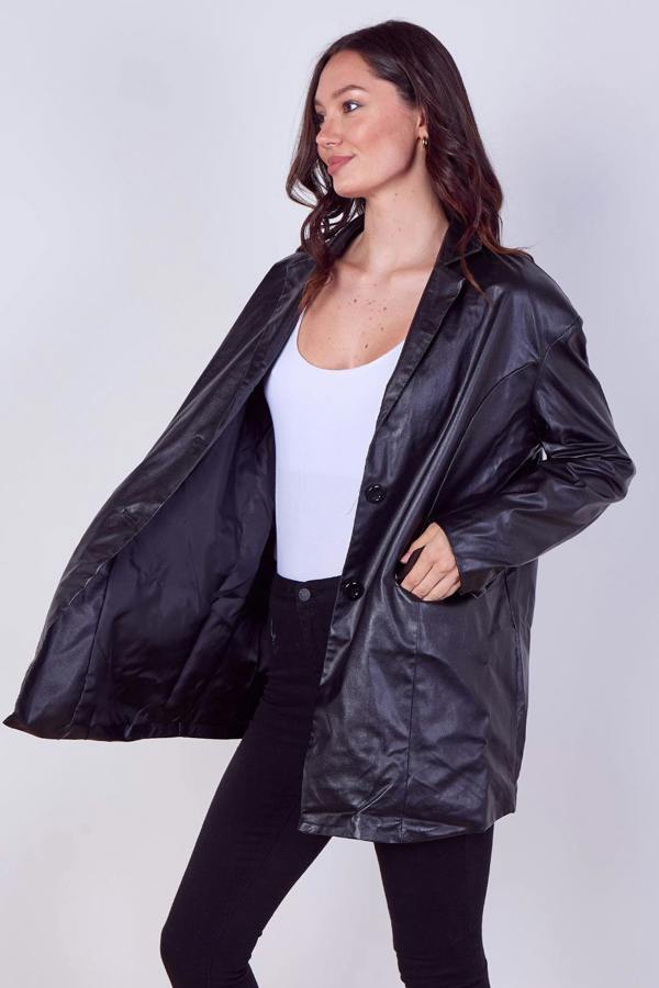 A woman modeling a black faux-leather jacket with a glossy finish, worn open over a white tank top and black pants, against a light gray studio background.