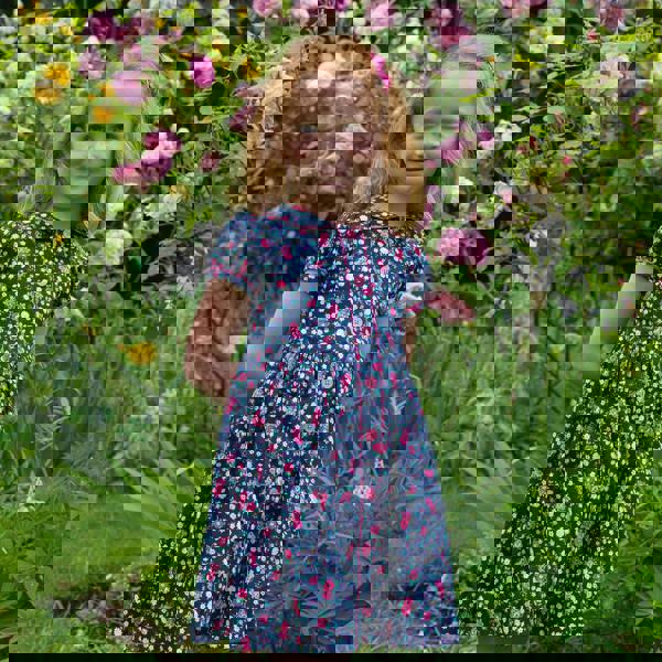 Girl in navy button-front dress with floral print, puff sleeves and pink ricrac trims and buttons.