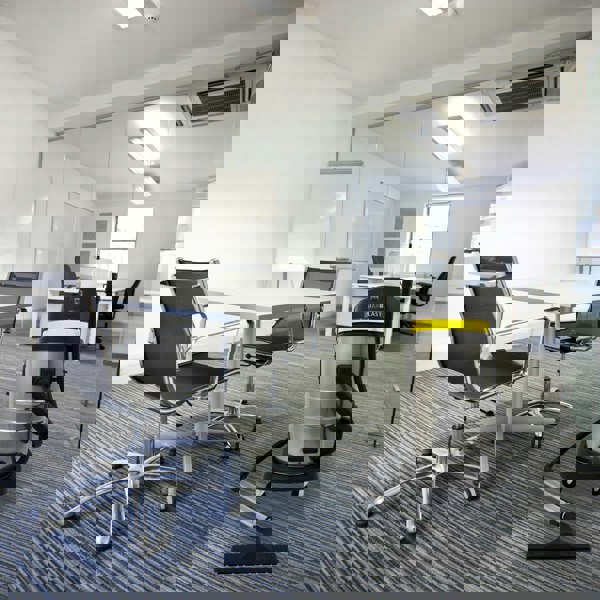 MAXBLAST 50L Industrial Vacuum Cleaner in a modern office setting, featuring a sleek silver body, black hose, and yellow accents