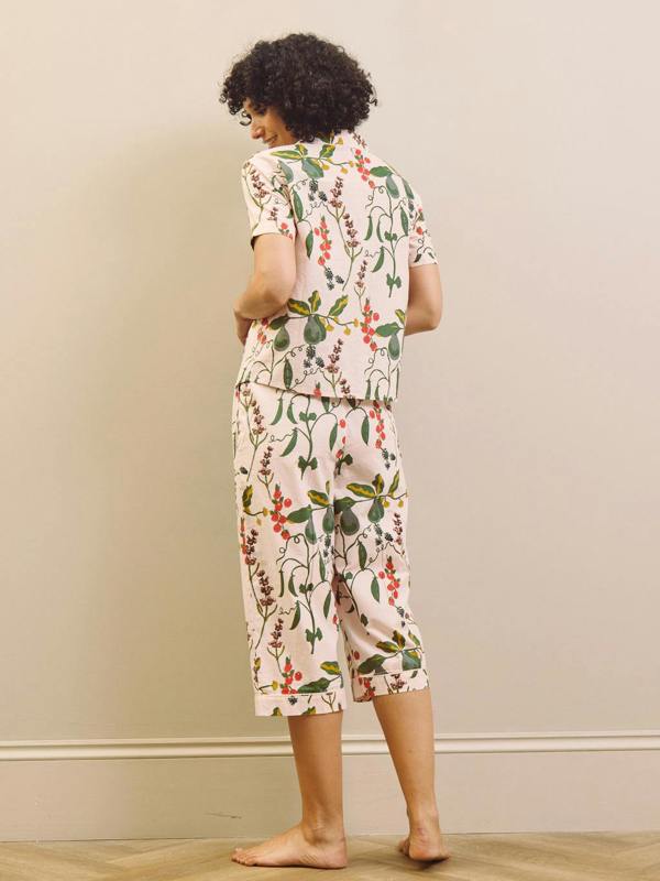 Woman wearing a pear & floral capri pyjama set against a plain wall.