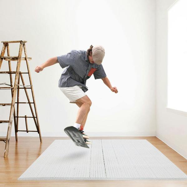 A person practicing ski trick indoors, jumping off the board on a white ski training mat mat in a minimal room with a ladder nearby.