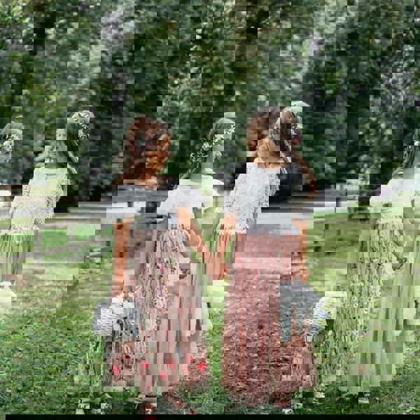 Two young girls in floral dresses holding hands in a park.