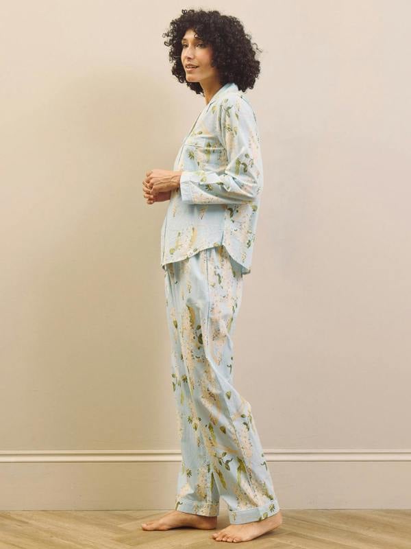 Woman wearing a light blue floral pyjama set against a beige wall.