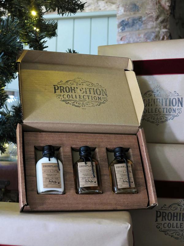 An open gift box from The Prohibition Collection containing three small bottles, shown with other branded boxes in the background.
